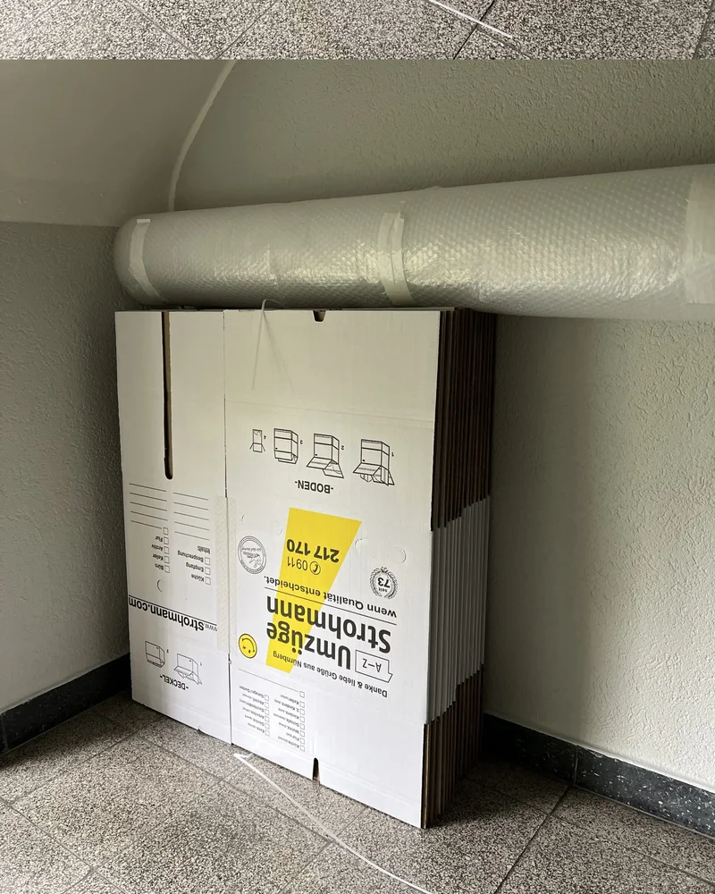 Stapel flach gefalteter Strohmann-Umzugskartons an einer Wand