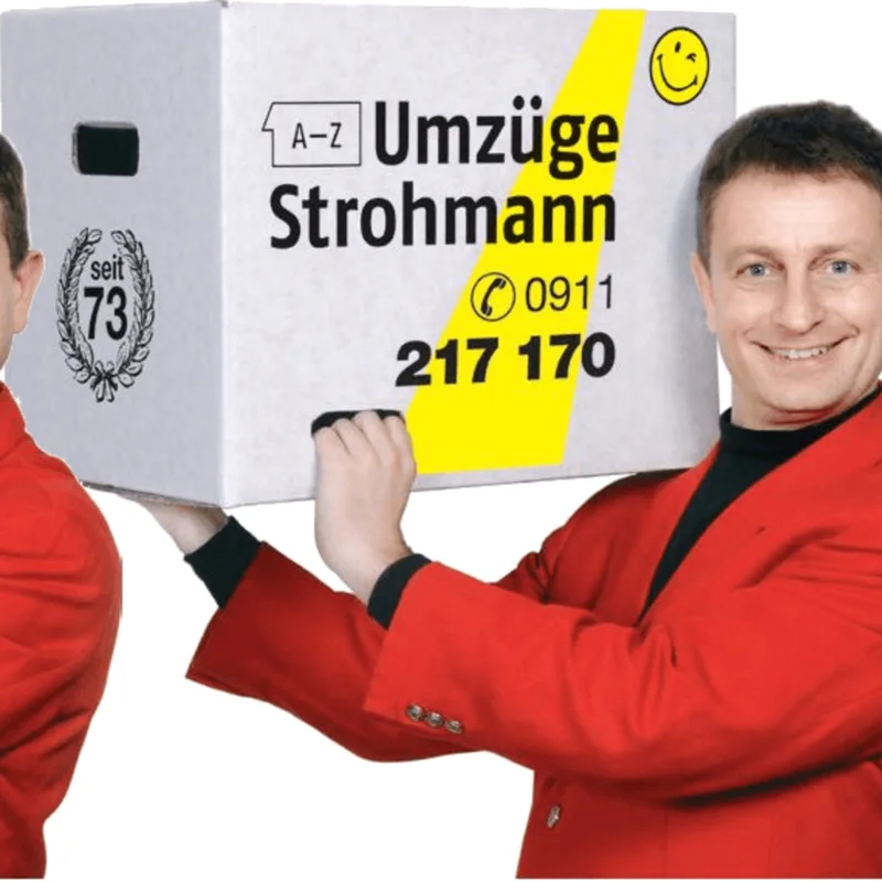 Thomas Kneißl im roten Sakko, einen Strohmann-Umzugskarton auf der Schulter